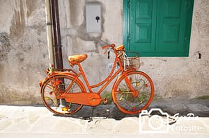 Oranges Fahrrad vor heller Wand mit grünen Fensterläden
